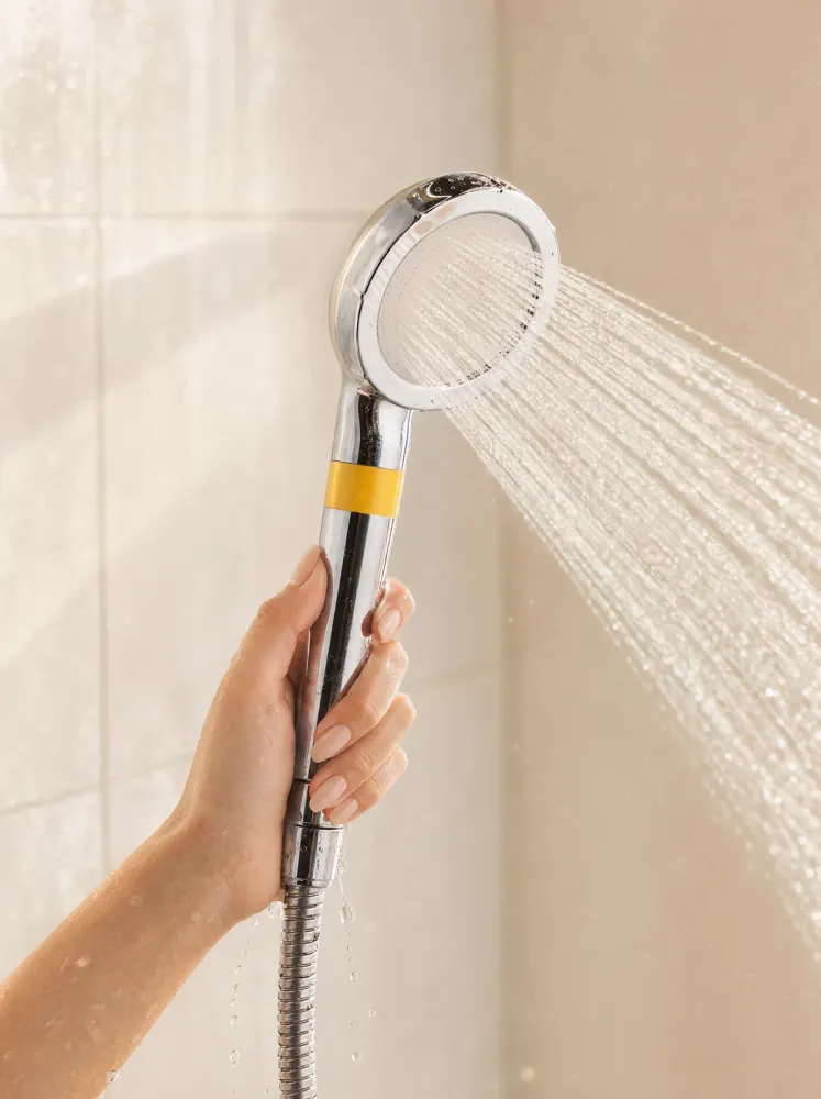 A hand holding the shower head under a running shower
